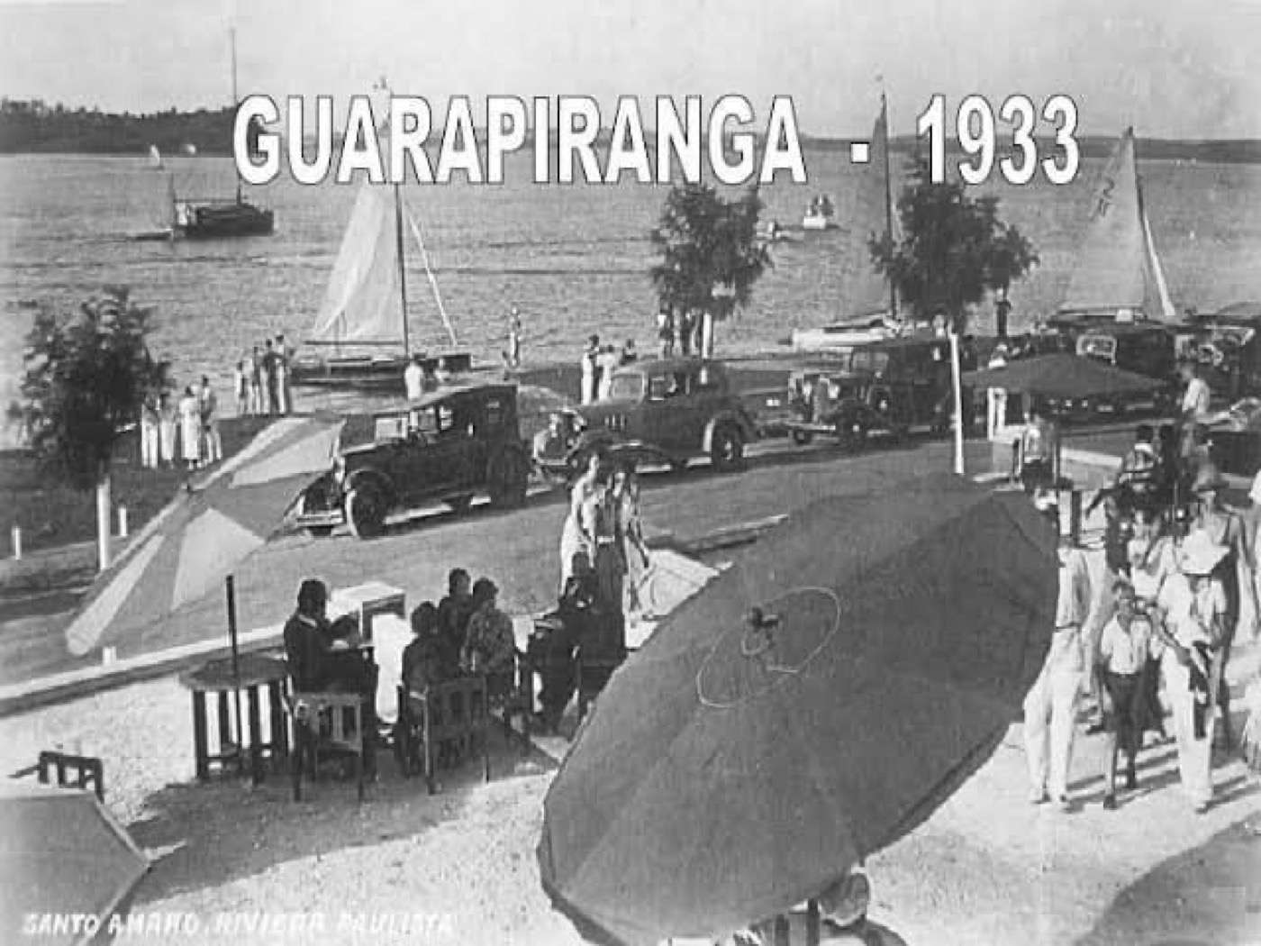 Orla da represa Guarapiranga em 1933, com carros antigos, veleiros e guarda-sóis